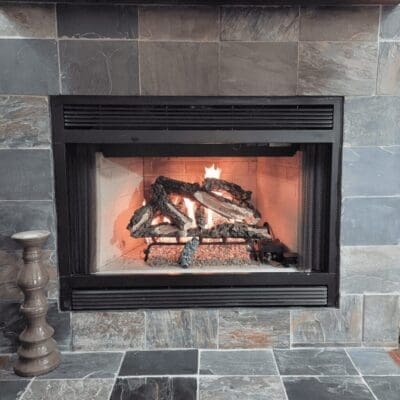 Cozy fireplace with burning logs inside a stone-tiled surround.